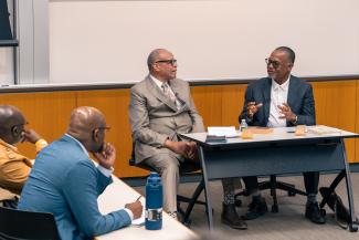 Bill Rhoden and Kenneth Shropshire talking to one another at a table as Kelly Harris and Wale Adebanwi watch and listen from audience seats