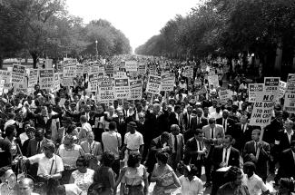 On Aug. 28, 1963, Martin Luther King Jr. (center left with arms raised) marches along Constitution Avenue in Washington, D.C., with other civil rights protestors carrying placards, from the Washington Monument to the Lincoln Memorial during the March on Washington. (Image: AP Photo)